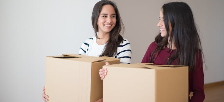 two young women holding boxes after they found out how to pack Christmas decorations for a move